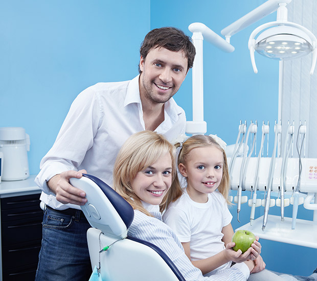 Male dentist smiling with a very young female patient and her mom