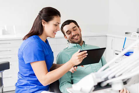 Young female dental assistant smiling as she shows a screen to a smiling male patient