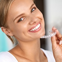 young female patient smiling and holding Invisalign aligners